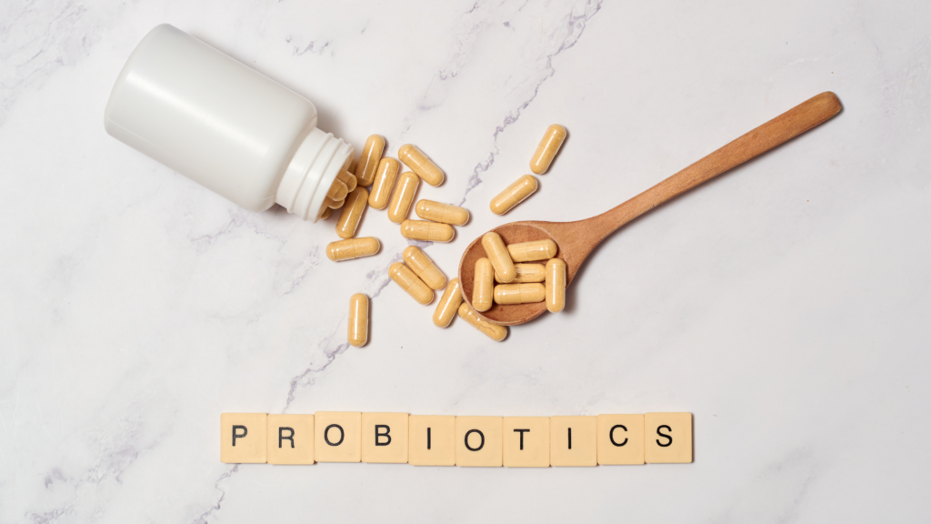 Probiotic capsules spilled from a bottle next to a wooden spoon, with the word “PROBIOTICS” spelled out below.